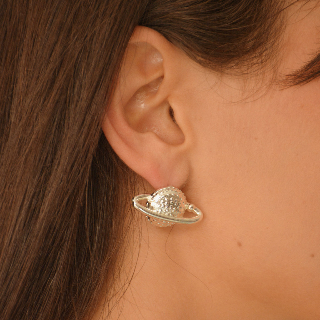 Aretes tipo topo en forma del planeta Saturno con acabado plateado en baño de plata ley 925.