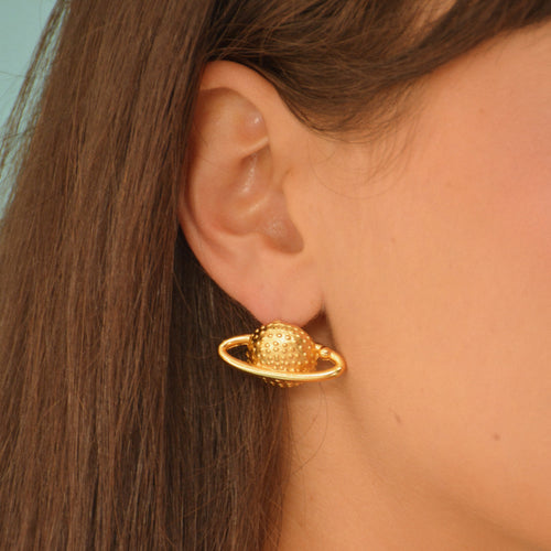 Aretes tipo topo en forma del planeta Saturno con acabado dorado en baño de oro de 24K.